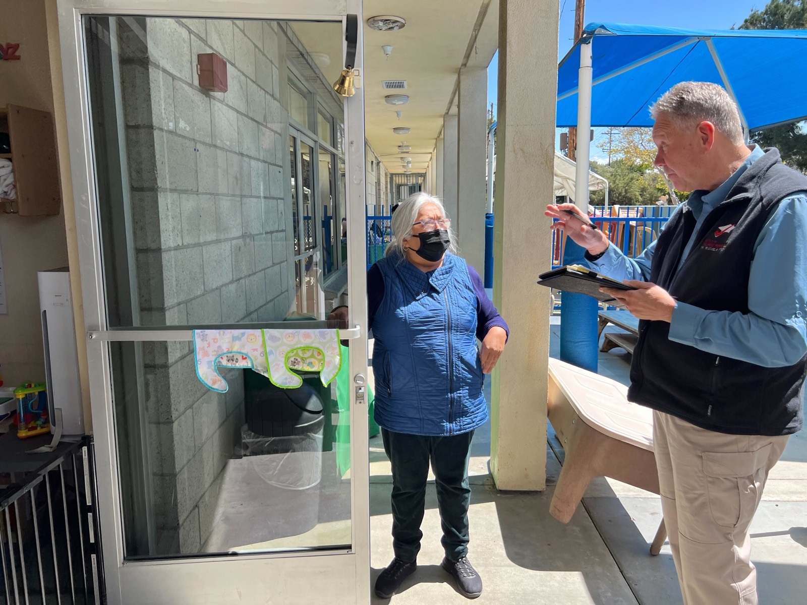 An ICP assessor with a tablet interviews a staff member at a childcare facility entrance